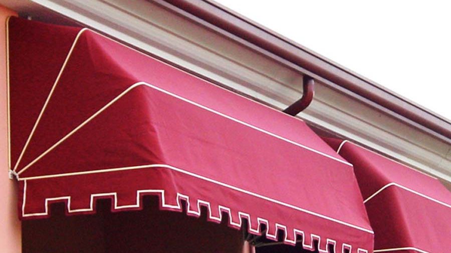 Toldo de capota de lona roja con faldón ondulado sobre el escaparate de un local
